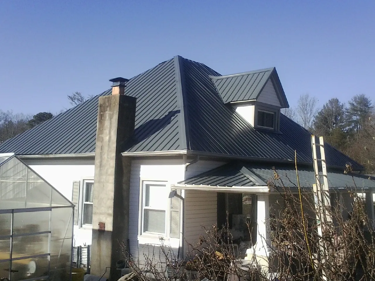 Dark blue standing seam metal roof on a white farmhouse with dormer — Slate & Tile Roof Repair by Roofing Brothers in Hannaford