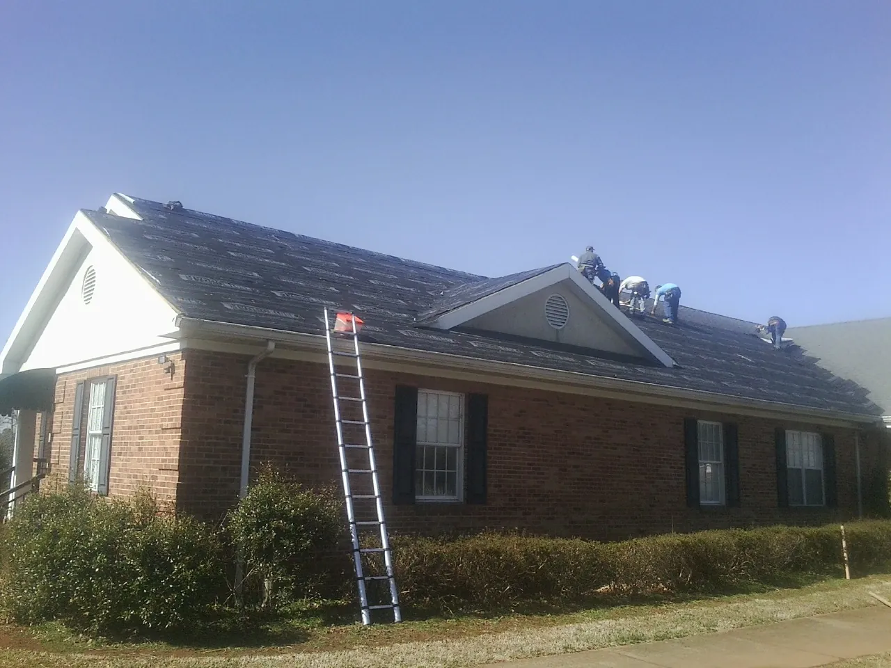 Crew tearing shingles off a brick ranch roof with a ladder set — Emergency Roof Repair work by our crew in Hannaford
