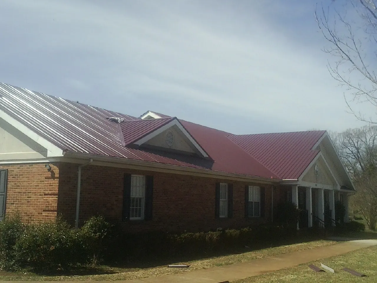 Red metal roof with gabled entries on a long brick building, from a Hail Damage Roof Repair job in Hannaford
