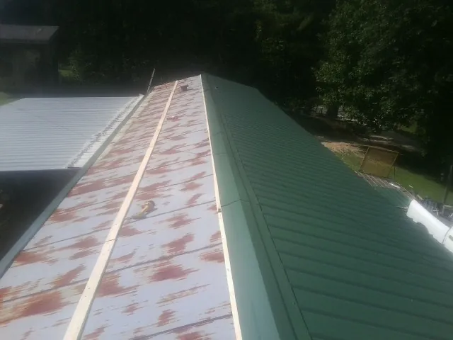 Old rusted panels beside newly installed green metal roofing — Wind Damage Roof Repair by Roofing Brothers in Hannaford