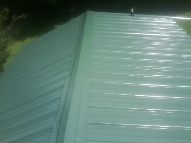 New green metal panels meeting at the ridge of a roof — Flat Roof Repair work by our crew in Hannaford