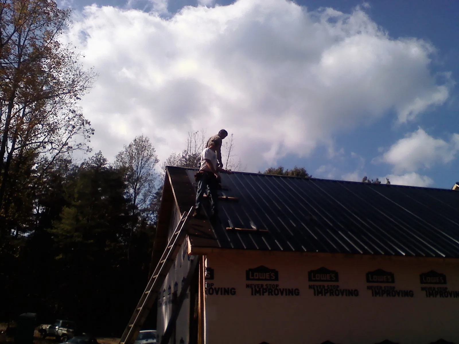 Roofer fastening dark metal panels high against a cloudy sky, from a Roof Inspection job in Hannaford