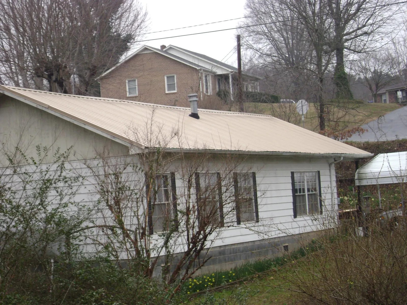 Tan metal roof on a white sided house set into a hillside — Commercial Roofing by Roofing Brothers in Hannaford