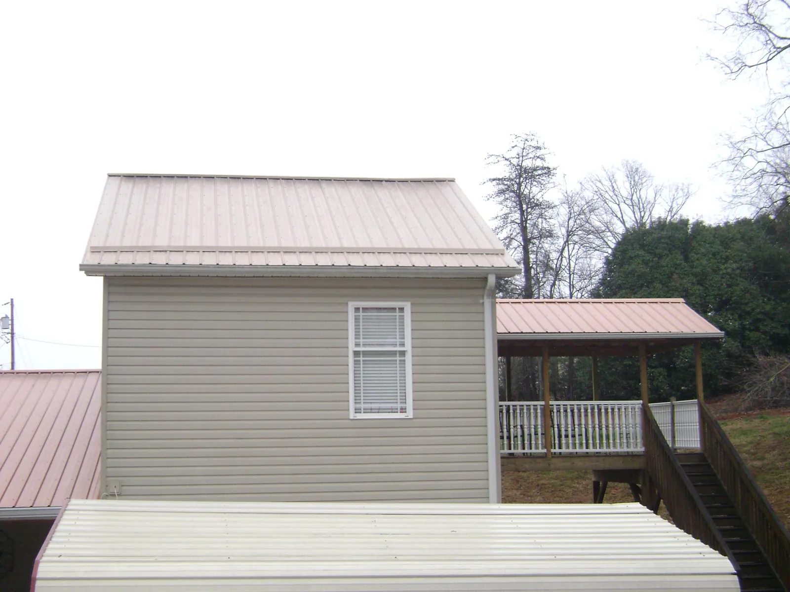 Tan metal roofs on a two story addition and attached porch, from a Roof Replacement job in Hannaford